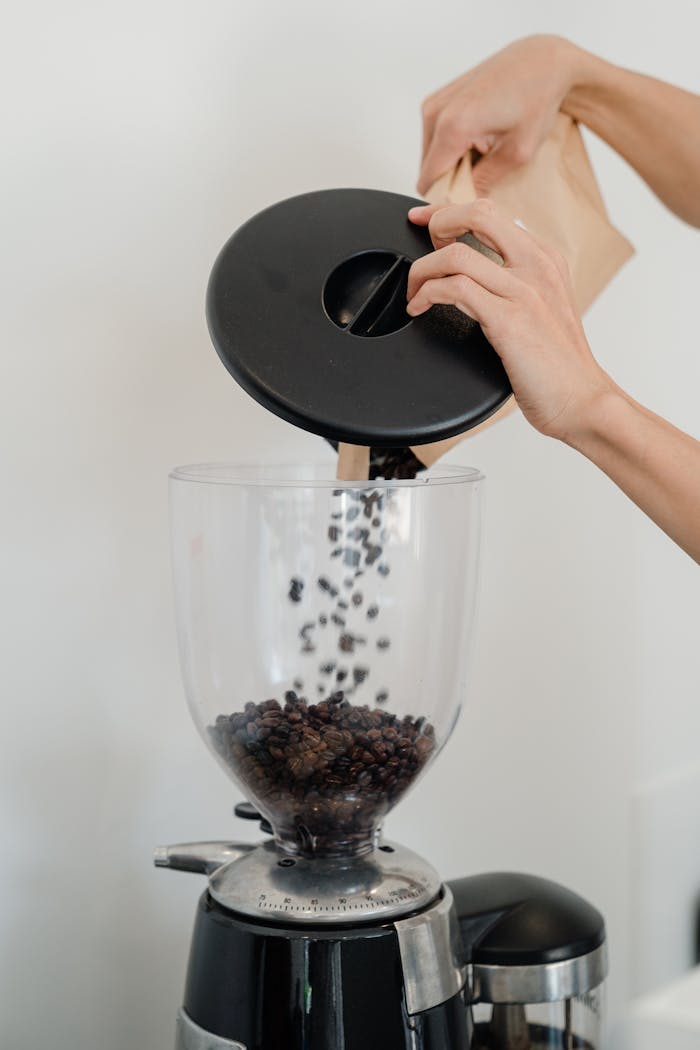 Close-up of hands pouring coffee beans into a grinder, preparing for a fresh brew.