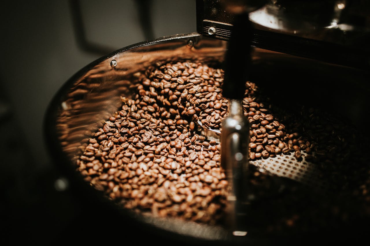 expertise-01 Close-up of freshly roasted coffee beans in a large industrial coffee roaster, showcasing rich textures and warm tones.